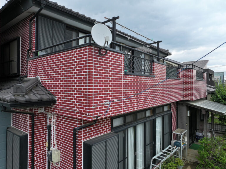 赤レンガ調に塗装した戸建て住宅の外壁。白い目地と黒いベランダ手すりが特徴的な施工後の外観
